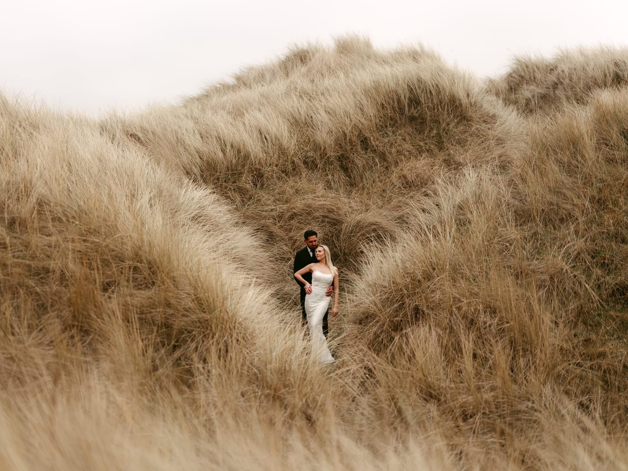 Das Brautpaar steht eng beieinander in einem geschützten Dünenkessel, umgeben von wildem Gras, fotografiert vom Hamburger Hochzeitsfotografen Sturmsucht